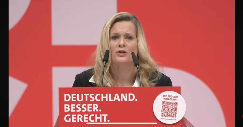 Ich Sie/IHR blond mittleres Alter hinter dem Rednerpult mit 2 Mikrofonen redend auf dem Pult steht Deutschland Besser Gerecht und ein QR-Code Rot weißer Hintergrund